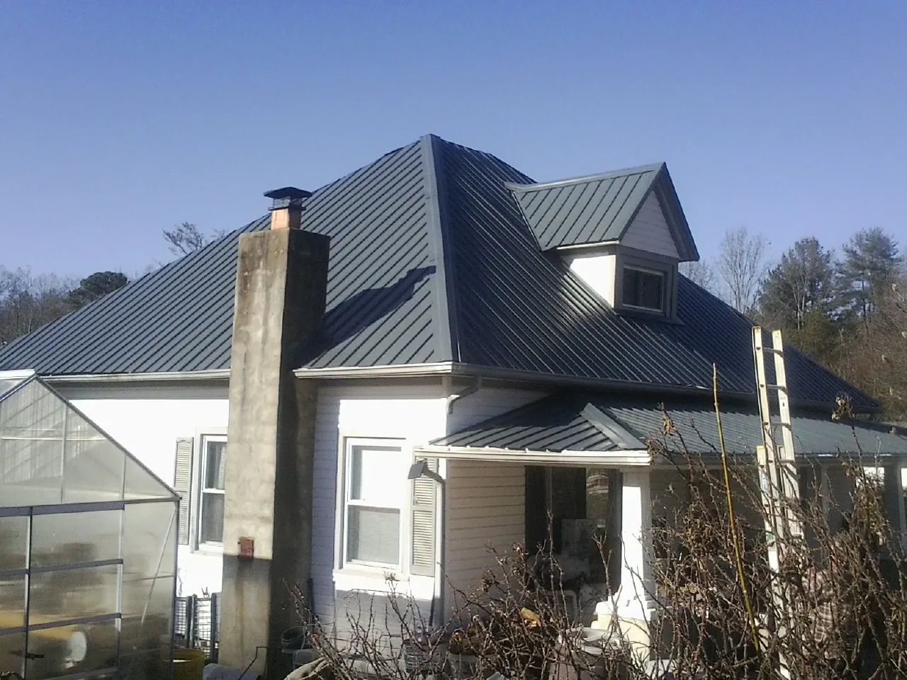 Dark blue standing seam metal roof on a white farmhouse with dormer — Slate & Tile Roof Repair by Roofing Brothers in South Beloit