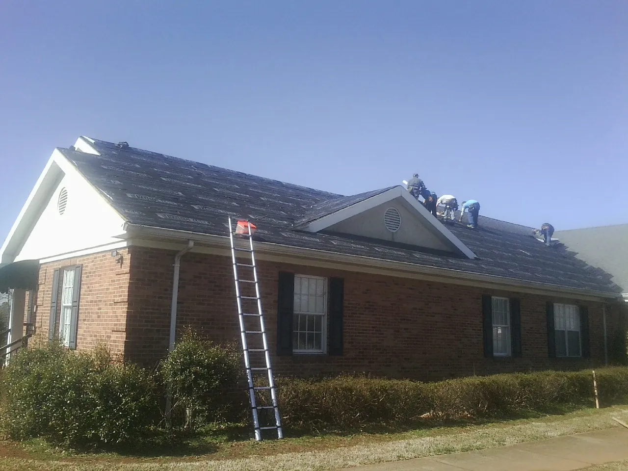 Crew tearing shingles off a brick ranch roof with a ladder set — Emergency Roof Repair work by our crew in South Beloit