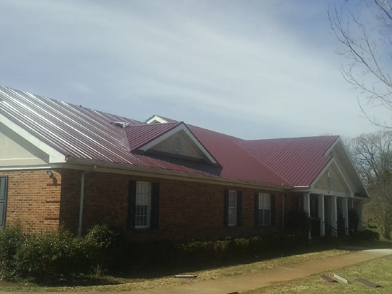 Red metal roof with gabled entries on a long brick building, from a Hail Damage Roof Repair job in South Beloit