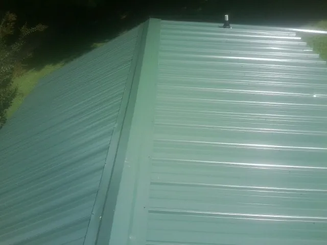 New green metal panels meeting at the ridge of a roof — Flat Roof Repair work by our crew in South Beloit
