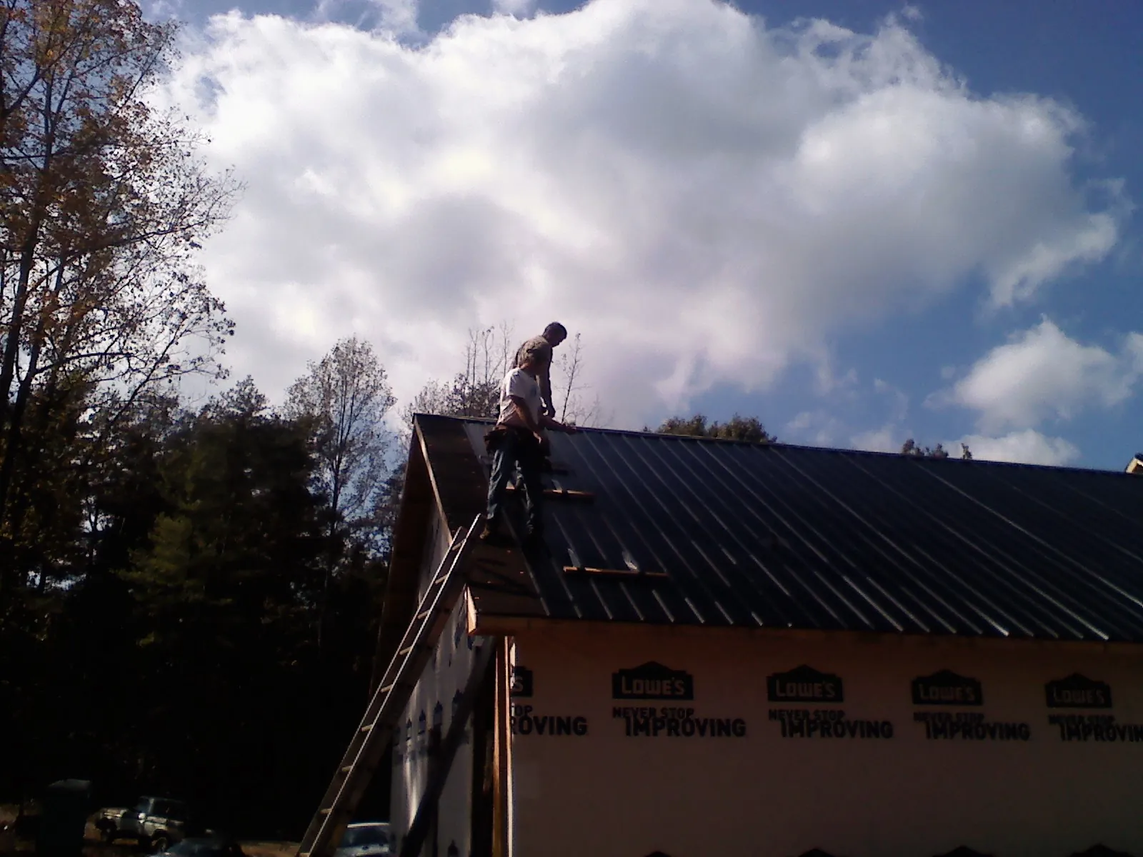 Roofer fastening dark metal panels high against a cloudy sky, from a Roof Inspection job in South Beloit