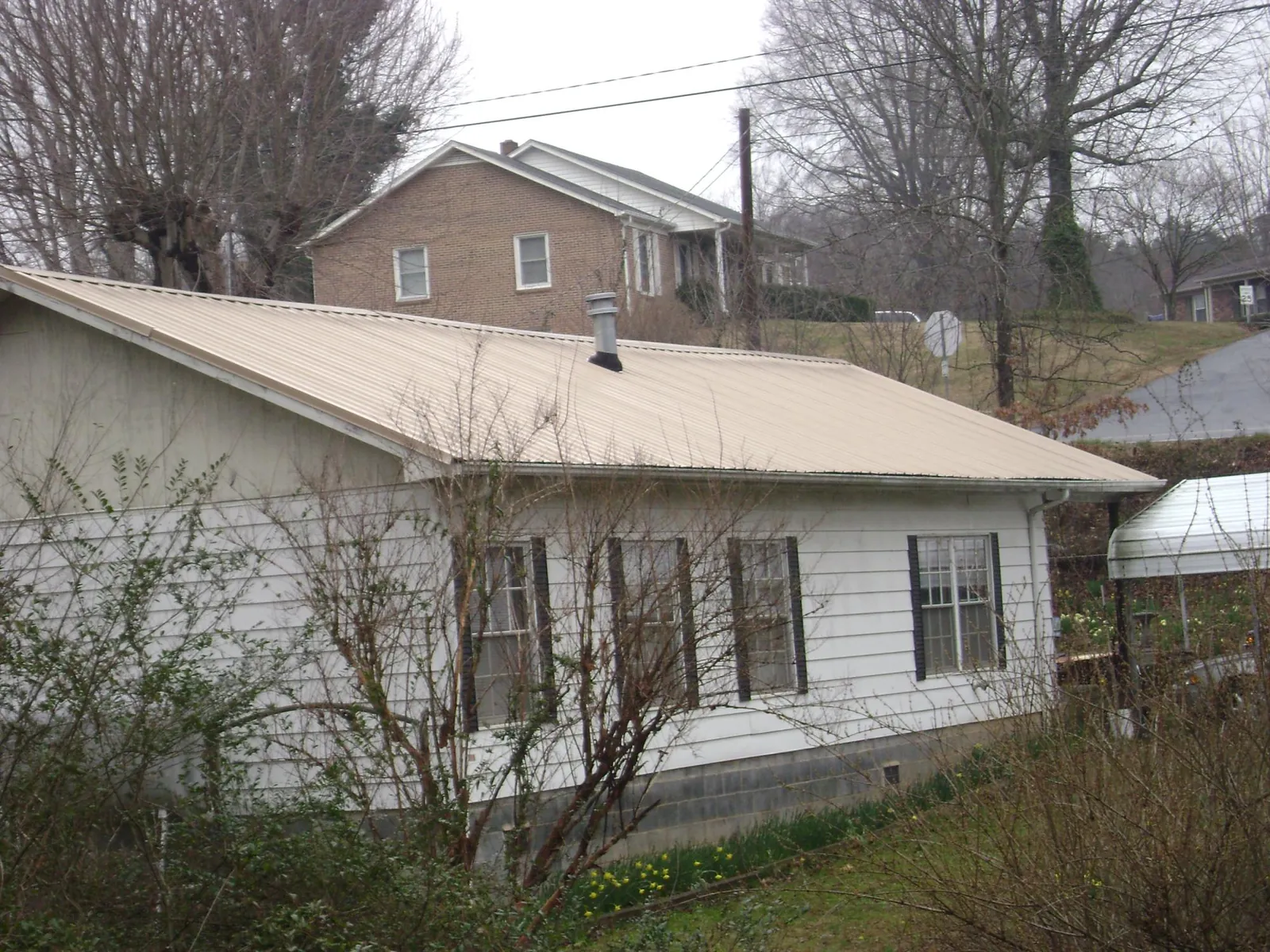 Tan metal roof on a white sided house set into a hillside — Commercial Roofing by Roofing Brothers in South Beloit